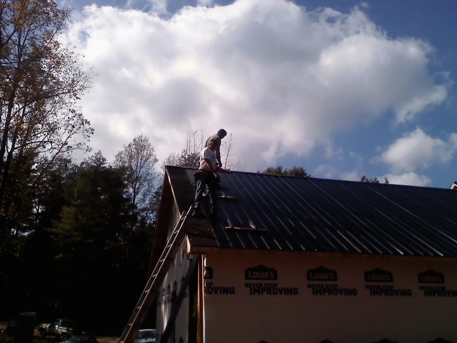 Roofer fastening dark metal panels high against a cloudy sky, from a Roof Inspection job in Louisville