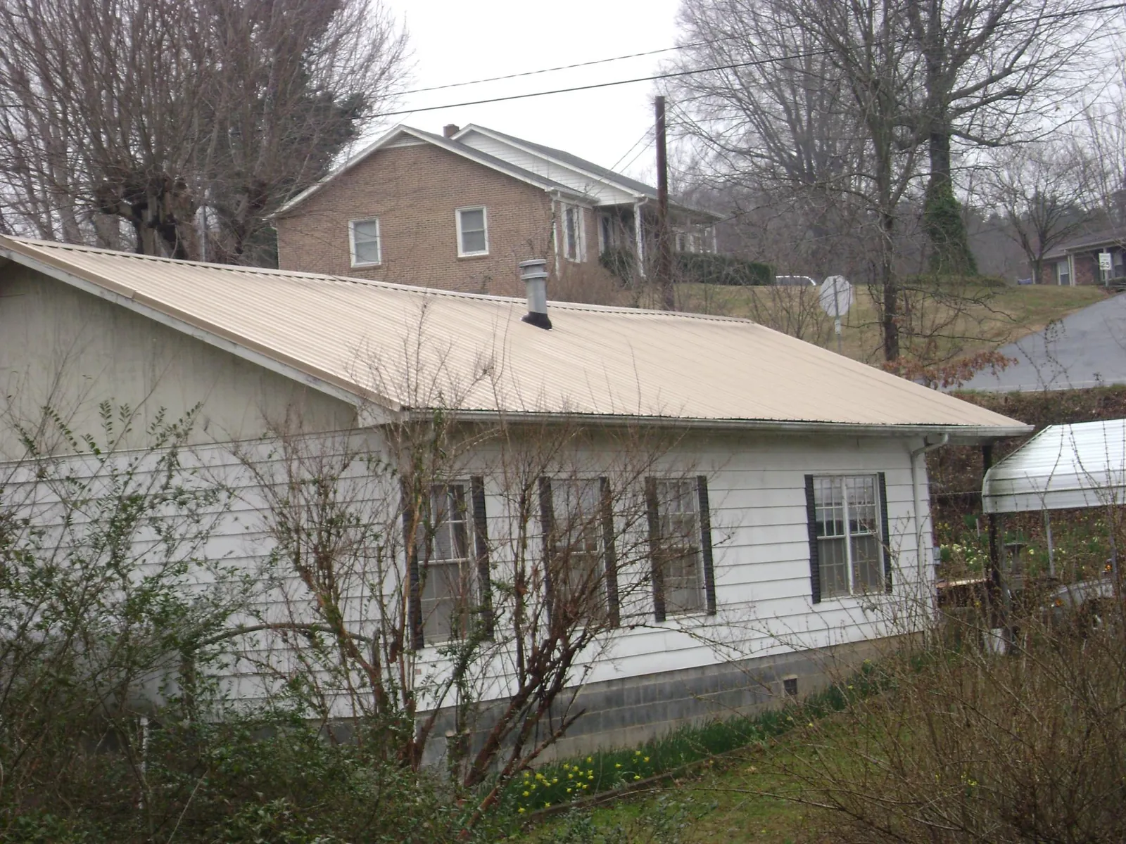 Tan metal roof on a white sided house set into a hillside — Commercial Roofing by Roofing Brothers in Louisville